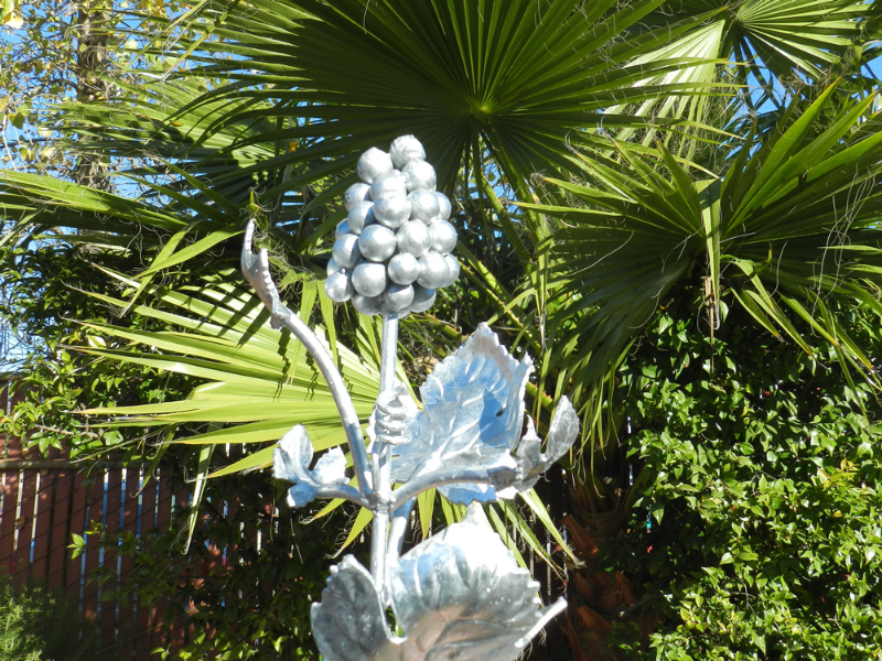 A decorative galvanized steel grapevine sculpture with leaves and a cluster of grapes